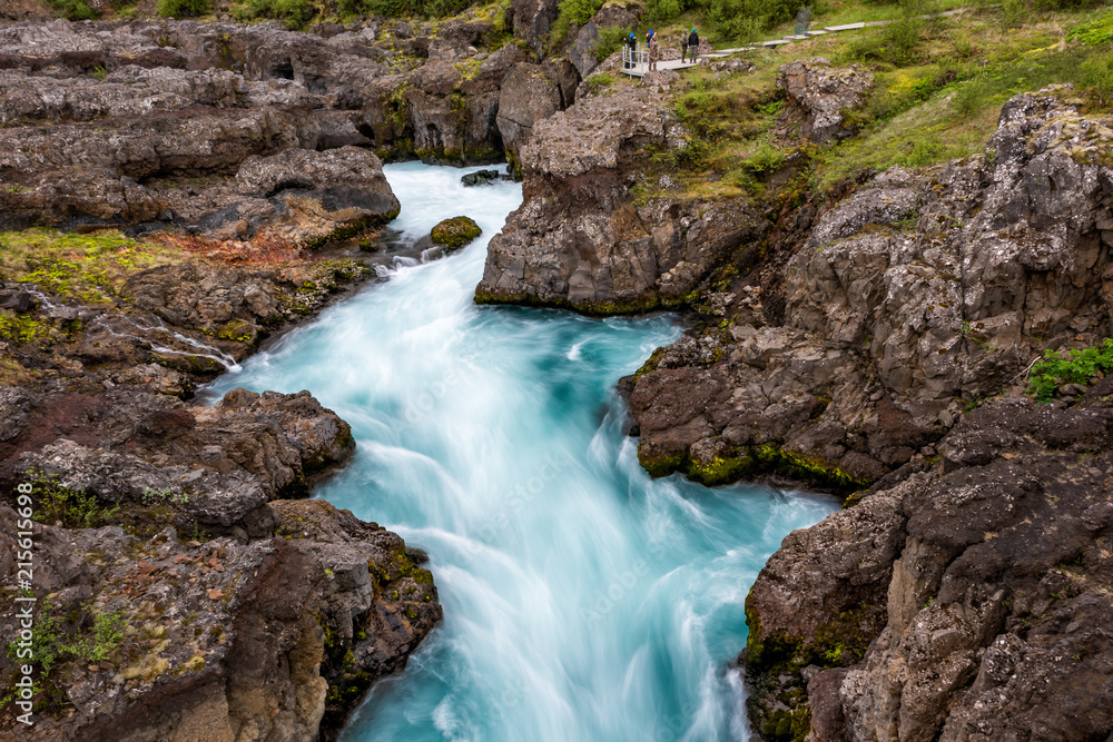 Obraz premium Long exposure smooth colorful blue aqua turquoise water waterfall cascade aerial view down of Hraunfossar Lava Falls in Iceland, landscape view