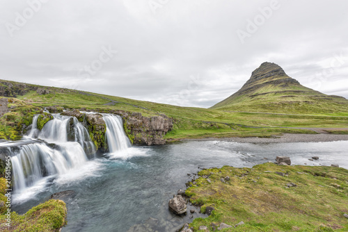 Landscape view of famous Kirkjufell Mountain and Waterfall landmark with long exposure smooth water wide angle with nobody  Grundarfjordur  green overcast cloudy day