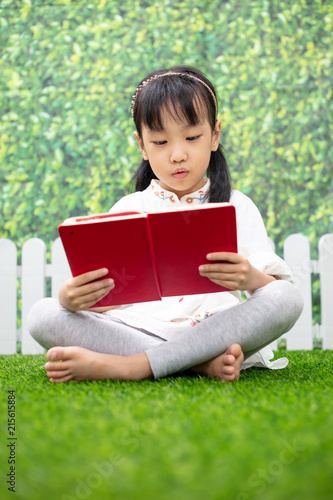 Asian Little Chinese girl sitting on the grass and reading book