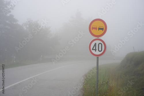 Traffic sign showing speed limit on misty road with poor visibility. Road through the foggy forest