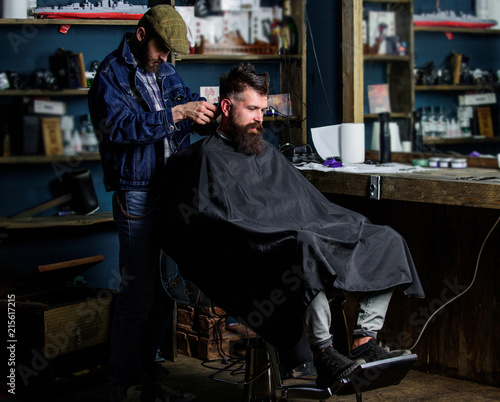 Barber with clipper trimming hair on nape of client. Hipster client getting haircut. Hipster style concept. Barber with hair clipper works on haircut of bearded guy barbershop background