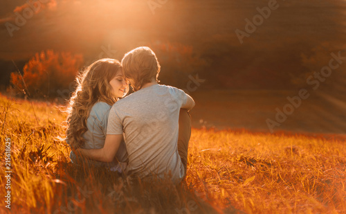 Stylish young couple sitting on a hill and admiring the sunset. A film photo with a light and a sunlight, a foreshortening from the back. Enamored youth in the second before the kiss photo