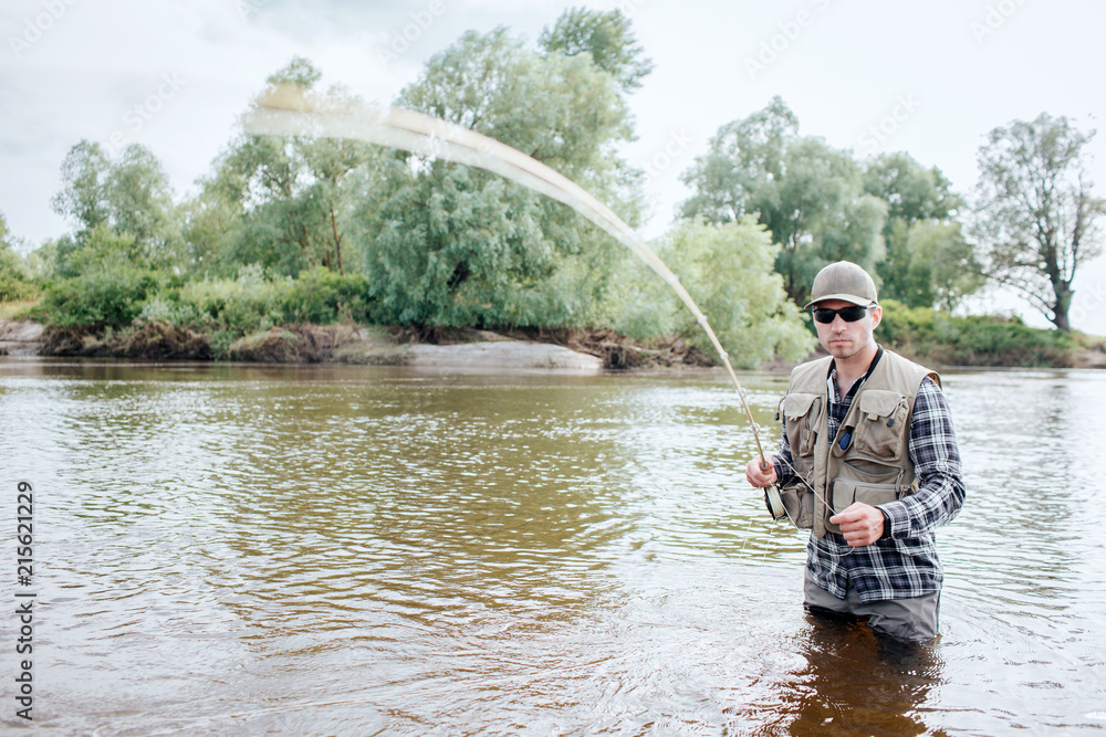 A picture of man holding fly rod. It is vibrating. Guy holds part of spoon in the other hand. He stands in water. He looks serious and cool.