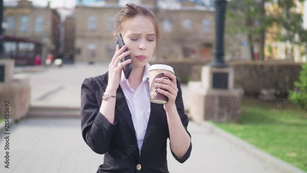 Beautiful brunette woman walking the city street and talking on the cell phone. Woman walking with coffee to go.