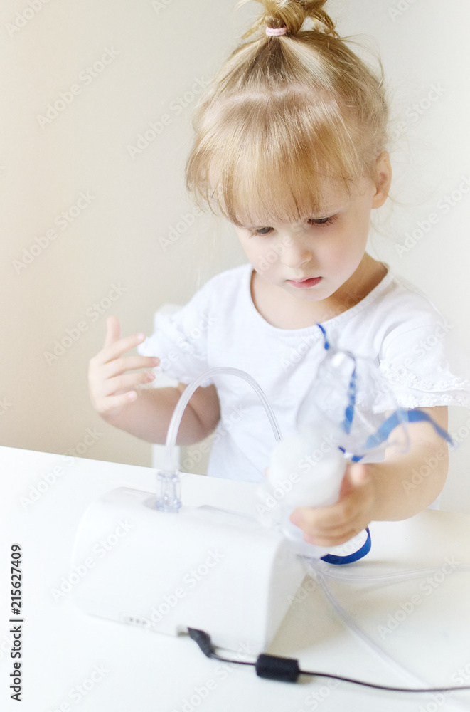Little girl in a mask for inhalations, making inhalation with nebulizer at home inhaler on the table, indoor, sick child Little girl in a mask for inhalations, making inhalation with nebulizer at home inhaler on the table, indoor, sick child