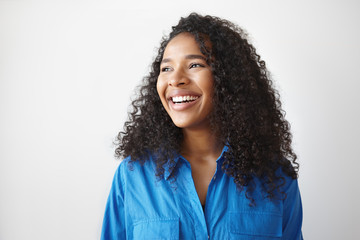 Positive human facial expressions, emotions, reaction and feelings. Attractive young dark skinned female with voluminous hairstyle laughing at joke, looking away, showing white perfect teeth