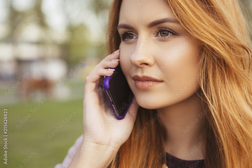 Red haired sexy plus size woman walking on a park. Cold weather, she wears leather jacket. She works on a phone, making calls Red haired sexy plus size woman walking on a park. Cold weather, she wears leather jacket. She works on a phone, making calls
