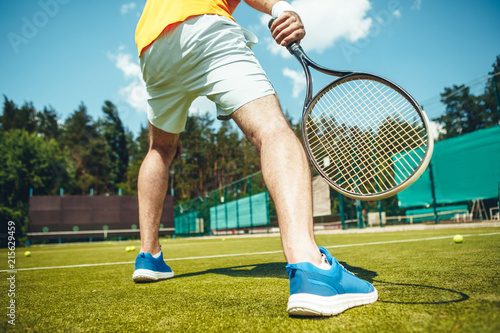 Low angle man legs standing on modern court. He practicing in tennis game in contemporary sneakers while keeping sport equipment photo