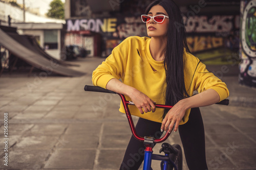 Sexy slim fit brunette woman in sport casual outfit in a skate park. Active leisure on a bicycle