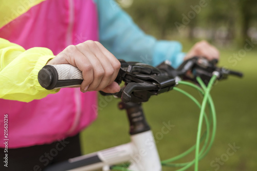 Young woman in sports wear relaxing in park after riding a bicycle. Fit, slim brunette woman with cheerful smile. Close up of a hands on a bicycle handlebars