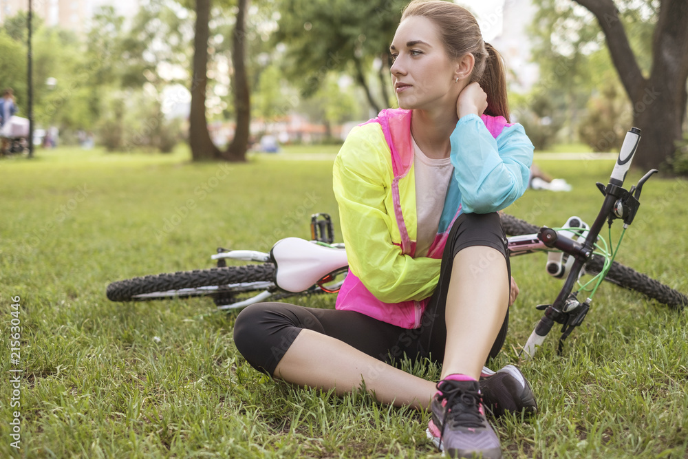 Young woman in sports wear relaxing in park after riding a bicycle. Fit,  slim brunette woman with cheerful smile. Summer weather, outdoors leisure.  Stock Photo | Adobe Stock