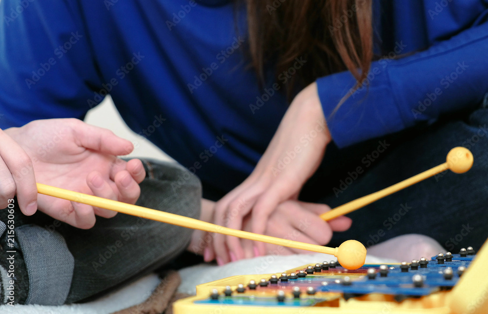 Playing music instrument. Closeup boy,s hand with stick playing on xylophone and his teacher sitting near him.
