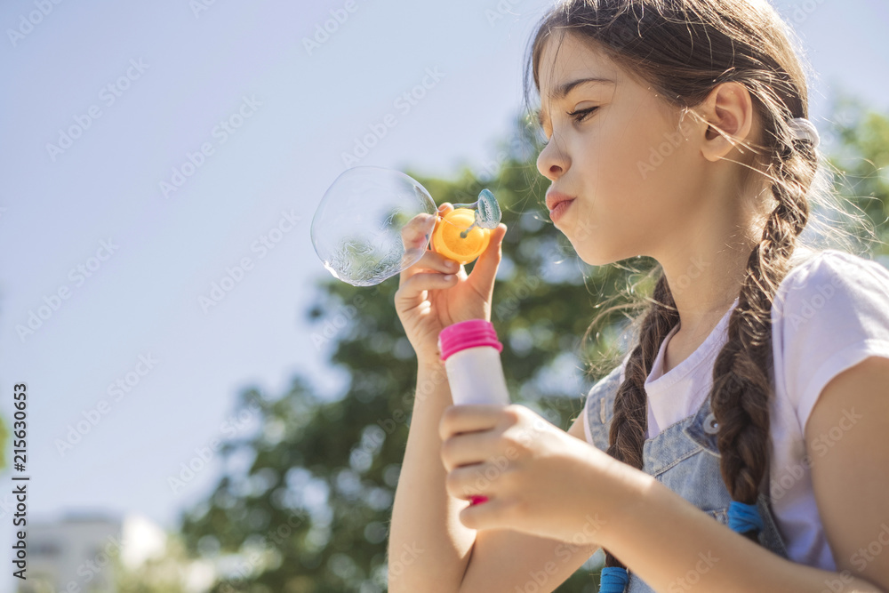 Cute little 10 years old girl in casual outfit playing at park in warm summer day. She blows soap bubbles. Copy space Cute little 10 years old girl in casual outfit playing at park in warm summer day. She blows soap bubbles. Copy space