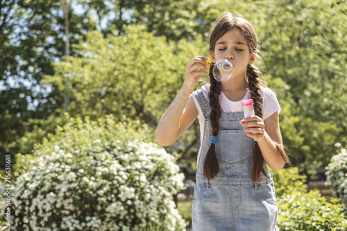 Wallpaper Mural Cute little 10 years old girl in casual outfit playing at park in warm summer day. She blows soap bubbles. Copy space Torontodigital.ca