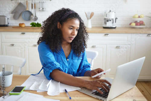 Fotografija Indoor shot of attractive serious young dark skinned with wavy hair doing paperw
