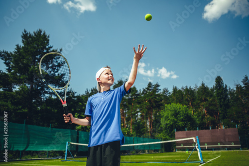 Side view smiling child catching ball while holding sport tool in hand. Glad kid playing tennis concept © Yakobchuk Olena