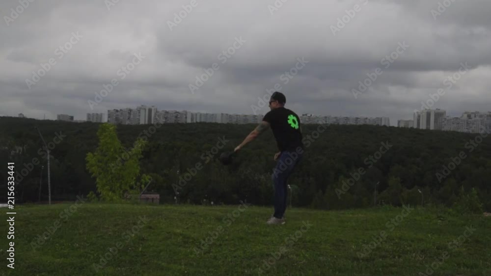 A man doing exercises with a weight on a hill overlooking the city. 120 FPS slow motion. A man doing exercises with a weight on a hill overlooking the city. 120 FPS slow motion.