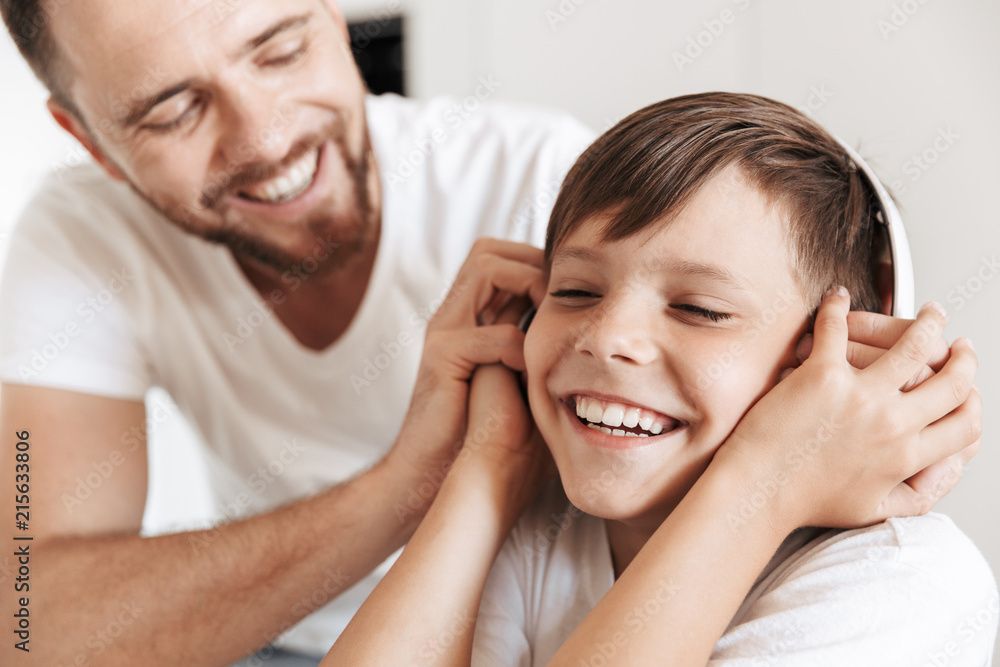 Portrait of happy boy 8-10 smiling and listening to music via wireless headphones, while resting at home with father Portrait of happy boy 8-10 smiling and listening to music via wireless headphones, while resting at home with father
