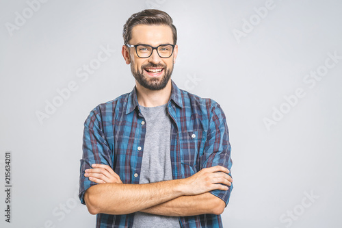 Happy young man. Portrait of handsome young man in casual shirt keeping arms crossed and smiling while standing against grey background photo