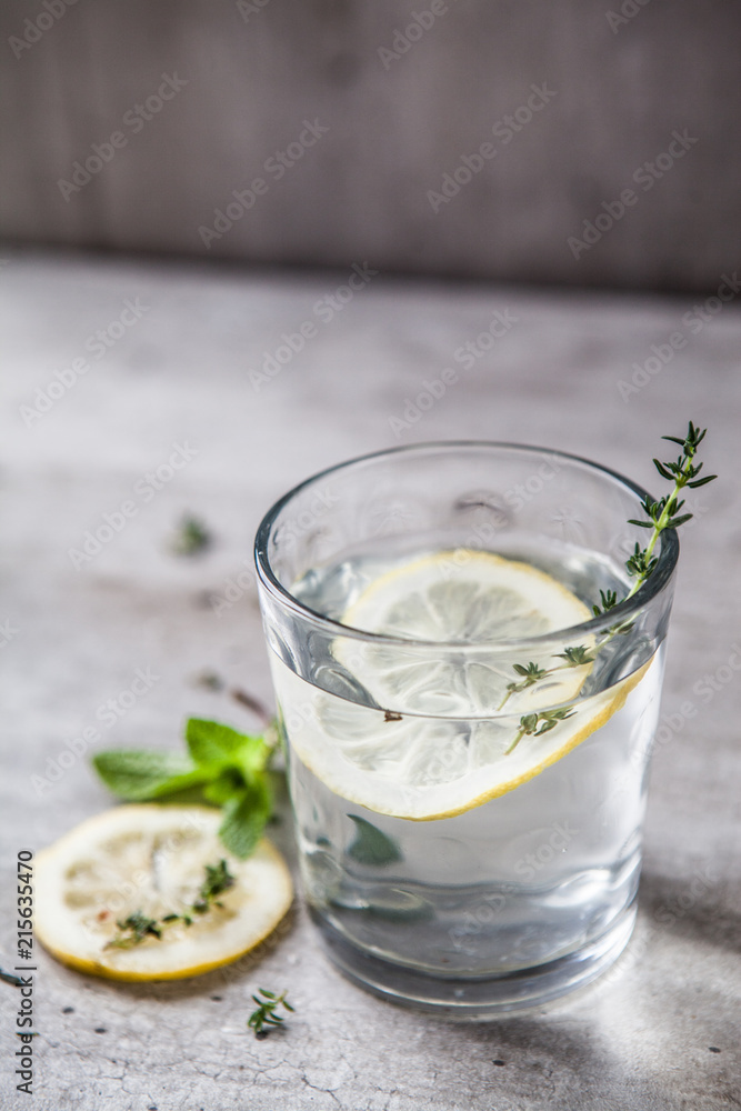 A glittering simple glass on a gray background with water, lemon and thyme A glittering simple glass on a gray background with water, lemon and thyme