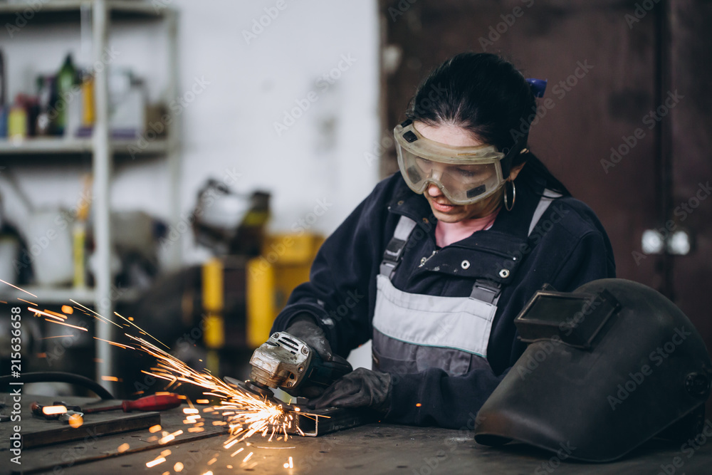 Strong and worthy woman doing hard job in car and motorcycle repair shop. She using grinder to fix some metal bike parts. Strong and worthy woman doing hard job in car and motorcycle repair shop. She using grinder to fix some metal bike parts.