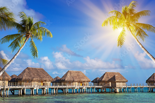 authentic houses with a straw roof over water and inclined palm trees over the sea. Polynesia.