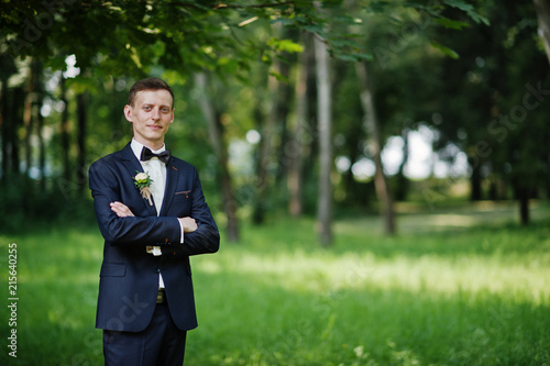 Portrait of a handsome groom posing alone in the park on the wedding day.