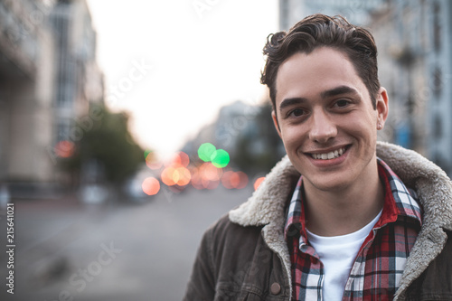 Waist up portrait of delighted young male standing on street and smiling.  He is happy to walk on his own. Copy space in left side photo