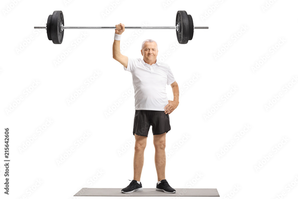 Mature man standing on an exercise mat and lifting a barbell with one hand Mature man standing on an exercise mat and lifting a barbell with one hand