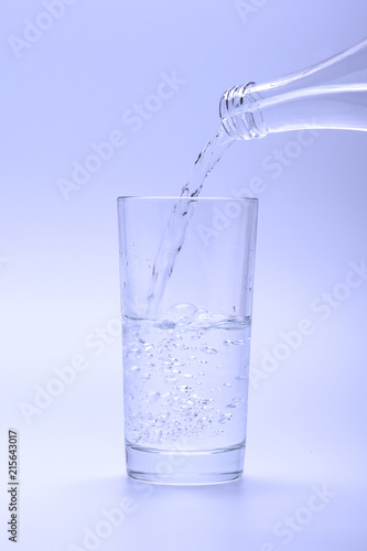 Pouring water into glass from a bottle, on white background