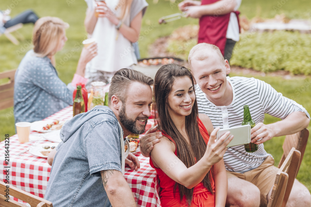 Fototapeta premium Smiling friends taking selfie during grill party in the garden