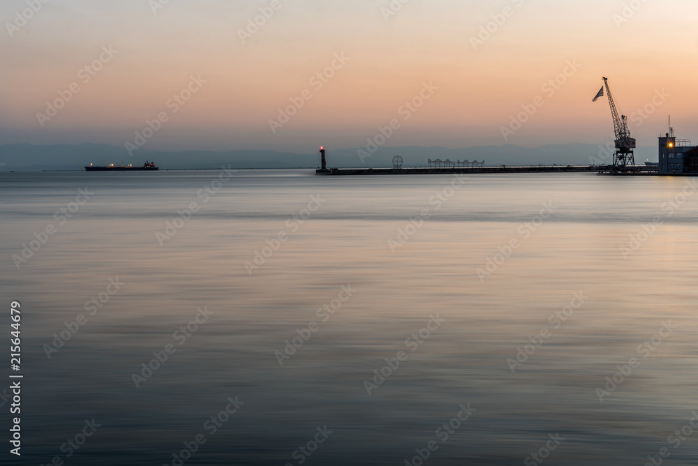 Thessaloniki Pier and Lighthouse at peaceful sunset, with a single ship in the background, Greece Thessaloniki Pier and Lighthouse at peaceful sunset, with a single ship in the background, Greece