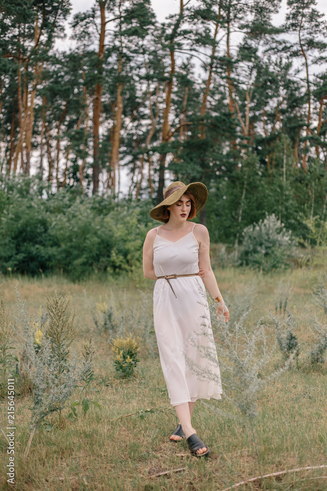 Beautiful red-haired girl in a dress and hat walking in a field Beautiful red-haired girl in a dress and hat walking in a field