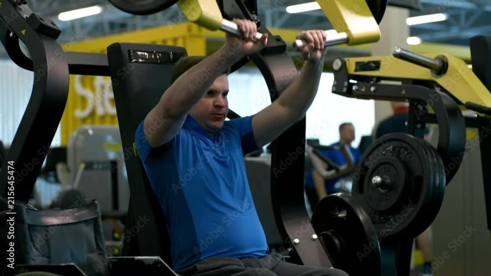 Tilt up of paraplegic man breathing hard and training on chest press machine in gym; wheelchair standing beside him Tilt up of paraplegic man breathing hard and training on chest press machine in gym; wheelchair standing beside him