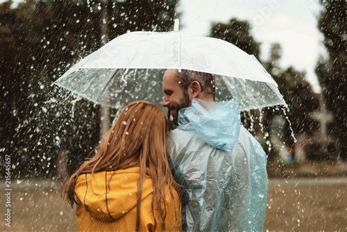 Smiling man walking side by side with woman under umbrella. They are enjoying nature together with content photo