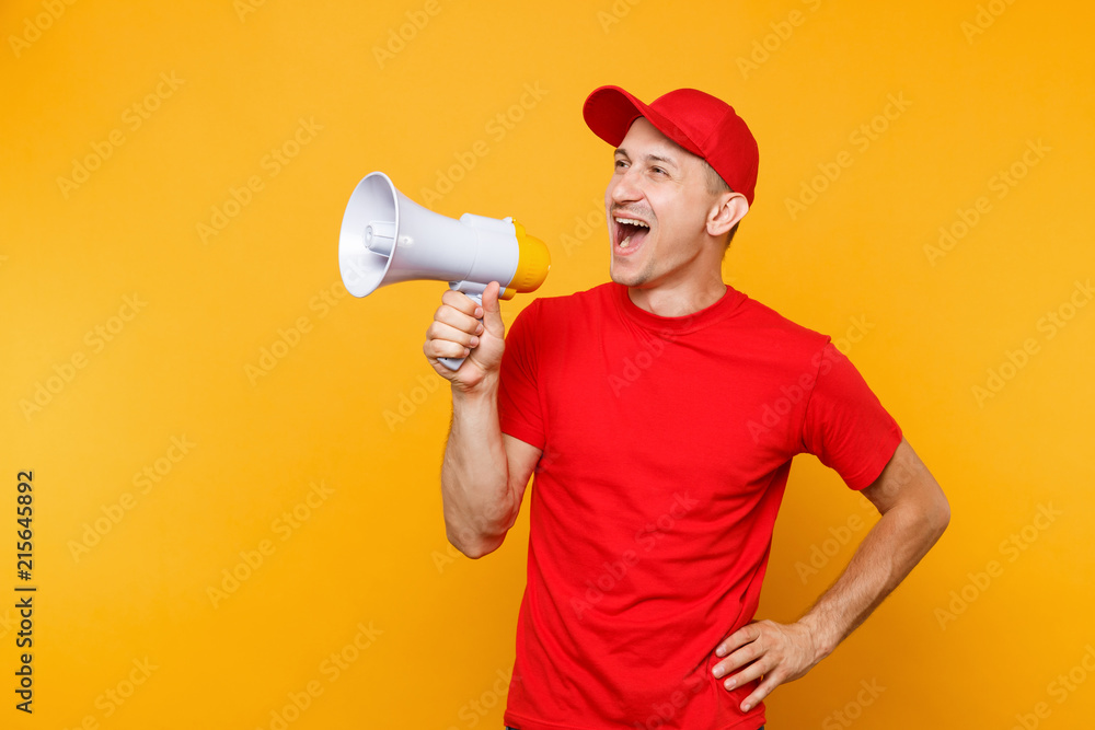 Delivery service man in red uniform isolated on yellow background. Male employee courier in cap, t-shirt screaming in megaphone hot news. Fun guy announces discounts sale. Copy space for advertisement Delivery service man in red uniform isolated on yellow background. Male employee courier in cap, t-shirt screaming in megaphone hot news. Fun guy announces discounts sale. Copy space for advertisement