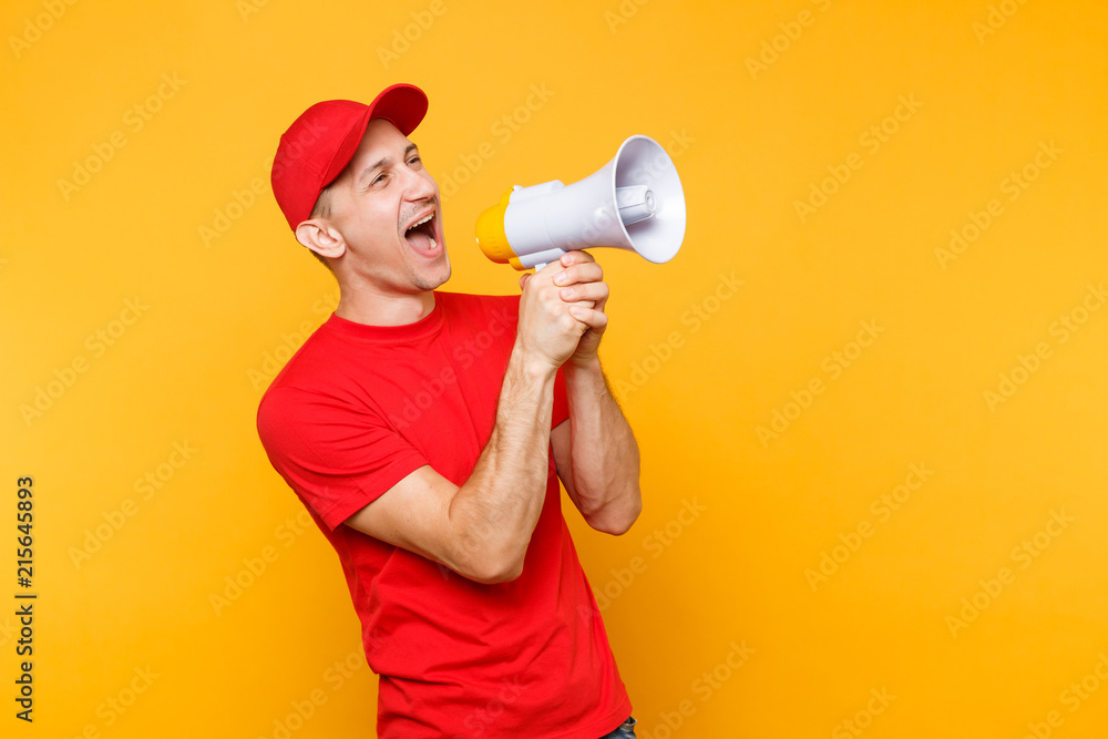 Delivery service man in red uniform isolated on yellow background. Male employee courier in cap, t-shirt screaming in megaphone hot news. Fun guy announces discounts sale. Copy space for advertisement Delivery service man in red uniform isolated on yellow background. Male employee courier in cap, t-shirt screaming in megaphone hot news. Fun guy announces discounts sale. Copy space for advertisement