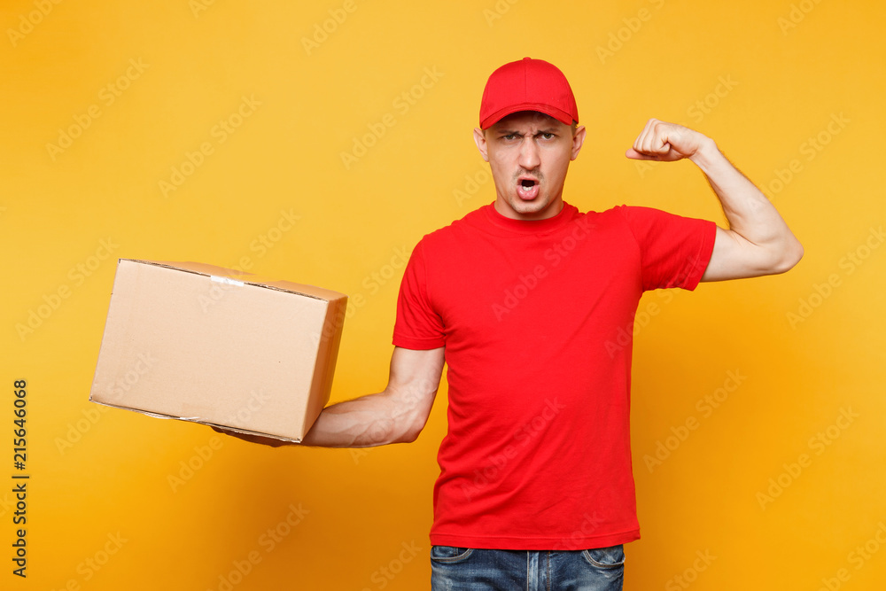 Delivery man in red uniform isolated on yellow orange background. Professional male employee courier or dealer in cap t-shirt holding empty cardboard box. Receiving package service concept. Copy space