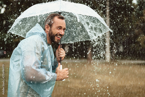 Εκτύπωση καμβά Side view of smiling happy man standing on grass and holding parasol