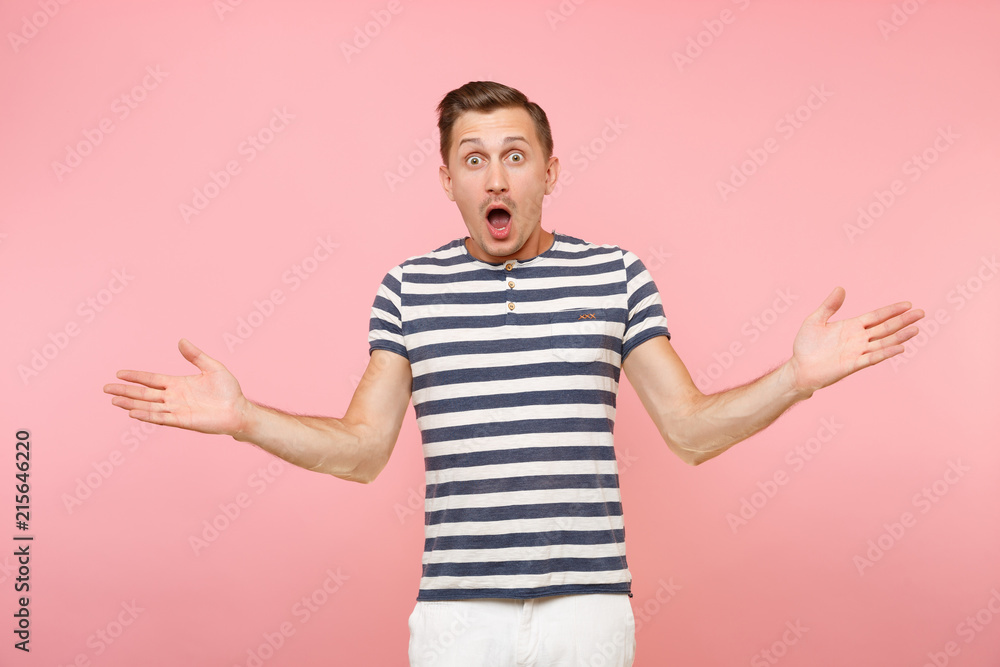 Portrait of surprised shocked man wearing striped t-shirt spreading hands gesture on copy space isolated on trending pastel pink background. People sincere emotions lifestyle concept. Advertising area Portrait of surprised shocked man wearing striped t-shirt spreading hands gesture on copy space isolated on trending pastel pink background. People sincere emotions lifestyle concept. Advertising area