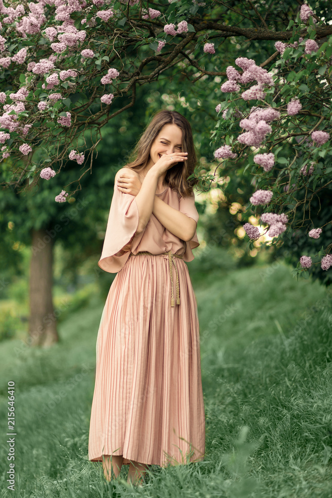 Young woman in a beautiful dress is standing near a lilac bush Young woman in a beautiful dress is standing near a lilac bush