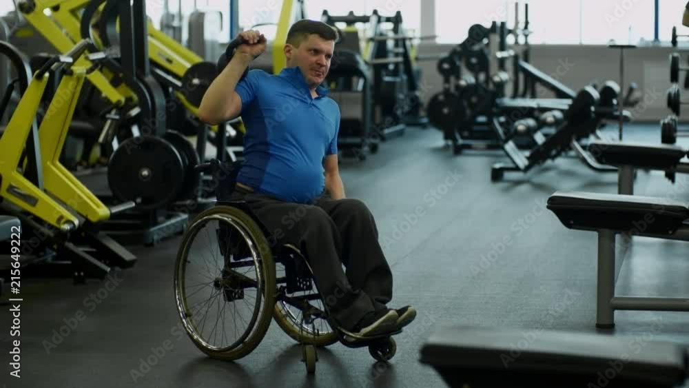 Tilt up of determined paraplegic man in wheelchair doing kettlebell shoulder press exercise in gym Tilt up of determined paraplegic man in wheelchair doing kettlebell shoulder press exercise in gym