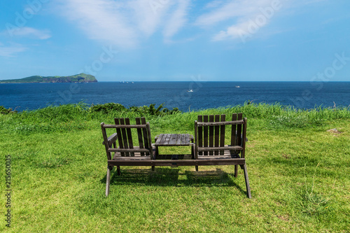 Wooden chairs on grass meadow with view on ocean and Udo Island, Jeju Island, South Korea