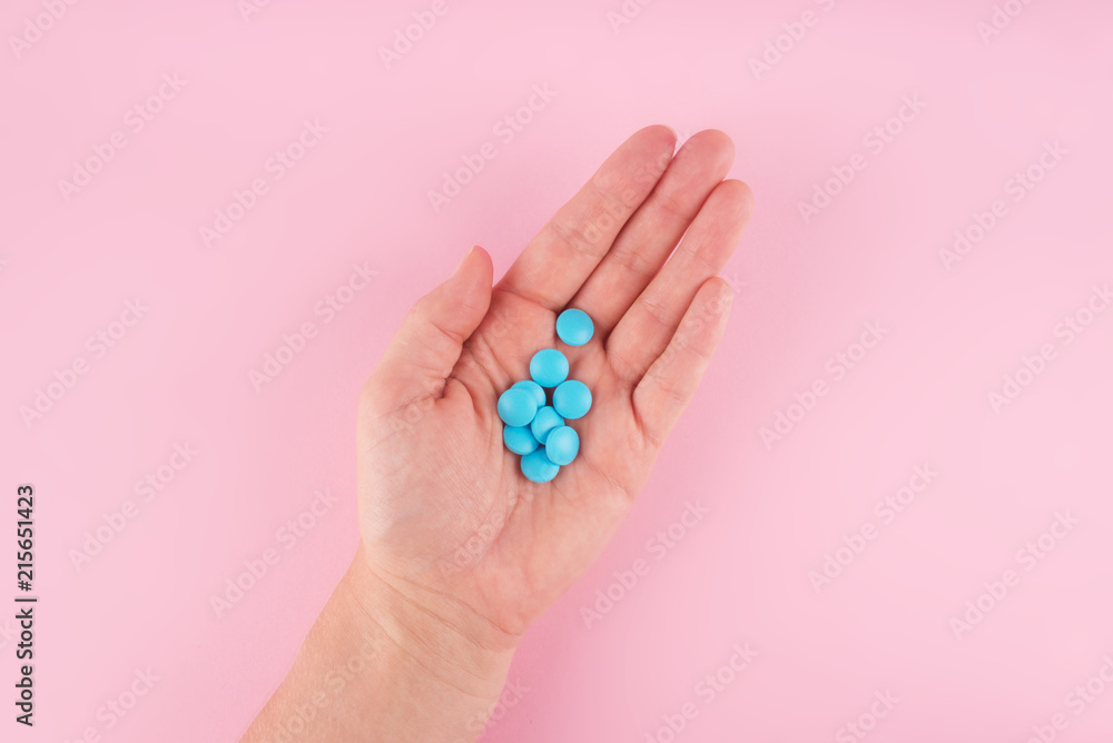 Hands hold blue pills isolated on pastel coloured background. Medication and prescription pills flat lay background. Hands hold blue pills isolated on pastel coloured background. Medication and prescription pills flat lay background.