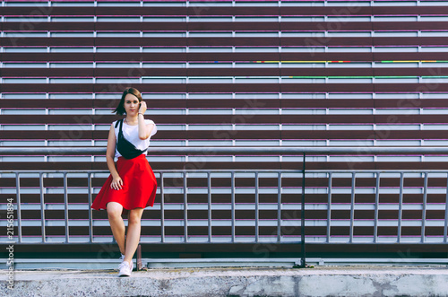 Fashionable young woman leaning back on fence in front of repetitive urban wall