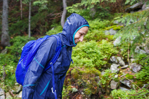 Happy hiker woman with backpack walking in rainy woods