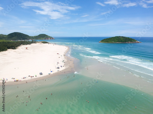  Aerial view of Brazilian beach with blue sky, white clouds, tourists in the sand, green and blue sea.