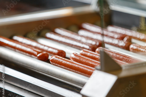 Greasy Hot dog sausages on turning cooking machine in cafe
