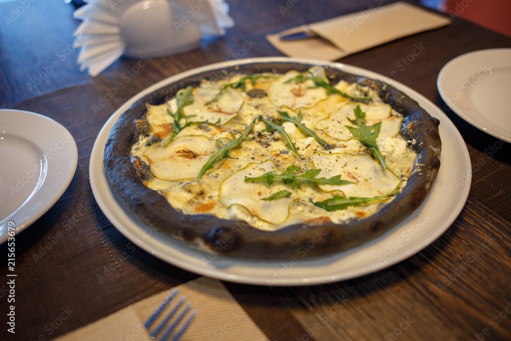 Black four cheese pizza served on the table in restaurant. Quattro formaggi pizza with pears on black dough Black four cheese pizza served on the table in restaurant. Quattro formaggi pizza with pears on black dough