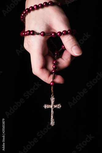 Rosary, cross   in female hands on a dark background. 